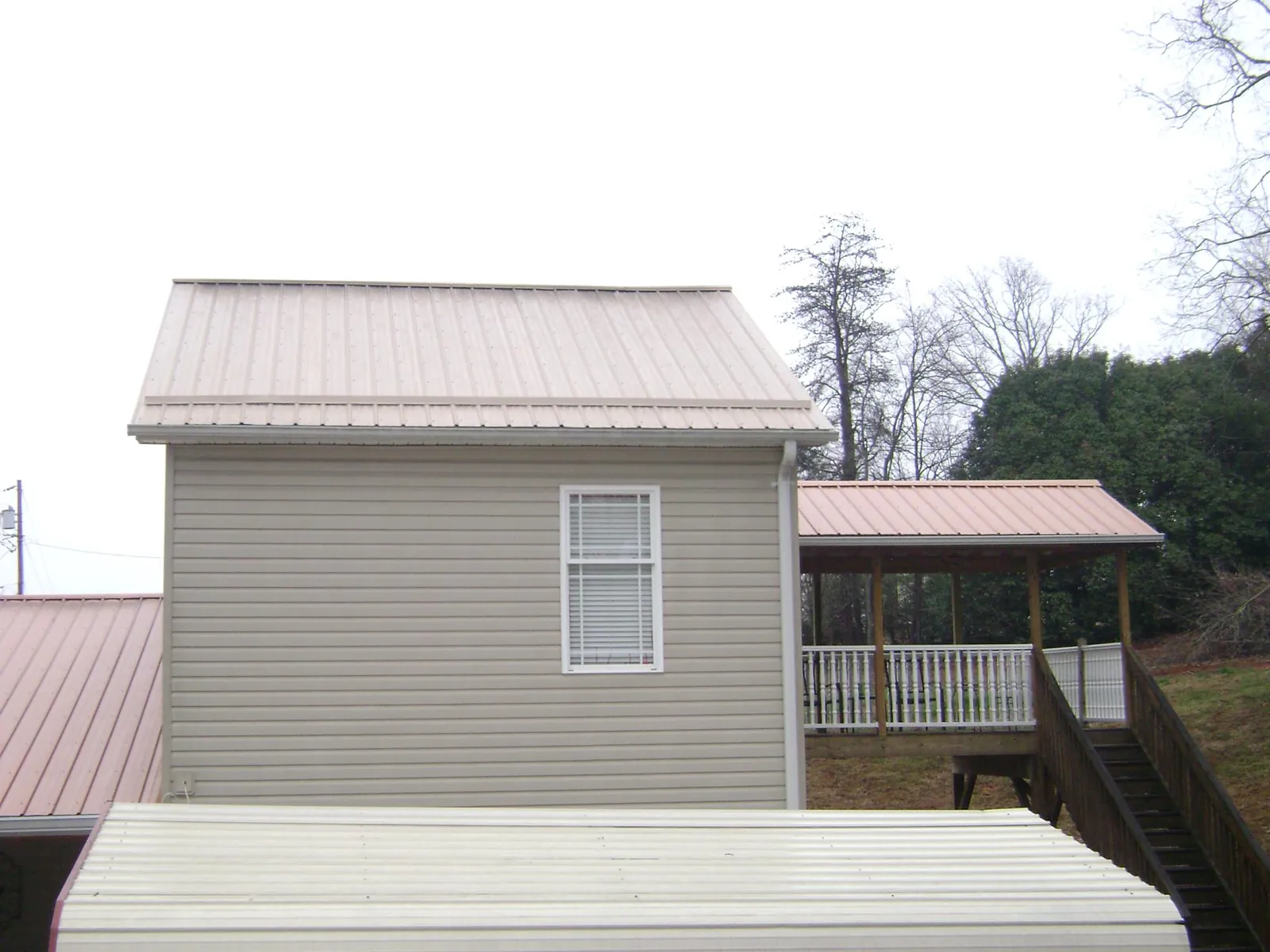 Tan metal roofs on a two story addition and attached porch, from a Roof Replacement job in Belmont